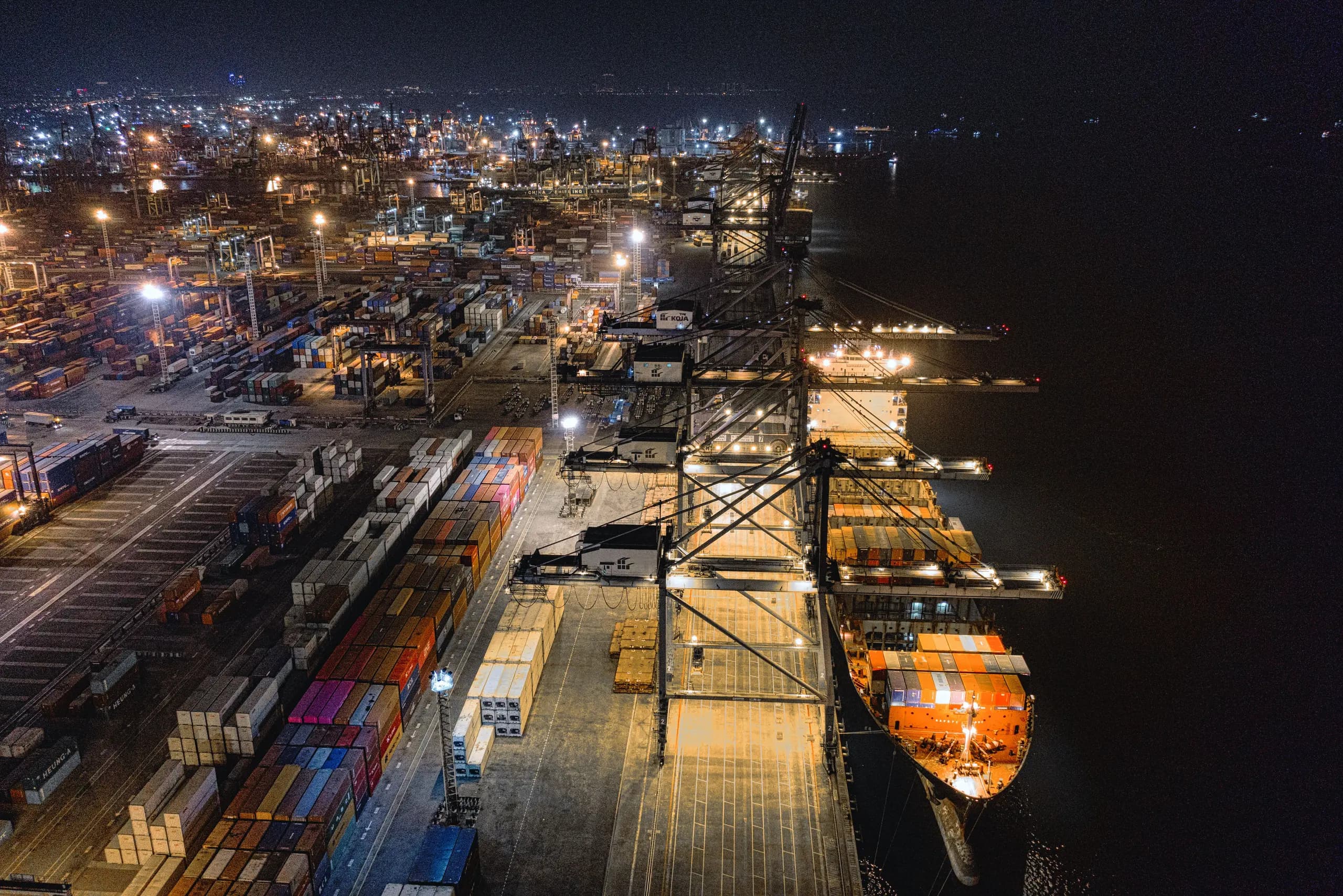 Container terminal at night, seen from above, with a vessel alongside under floodlit gantry cranes
